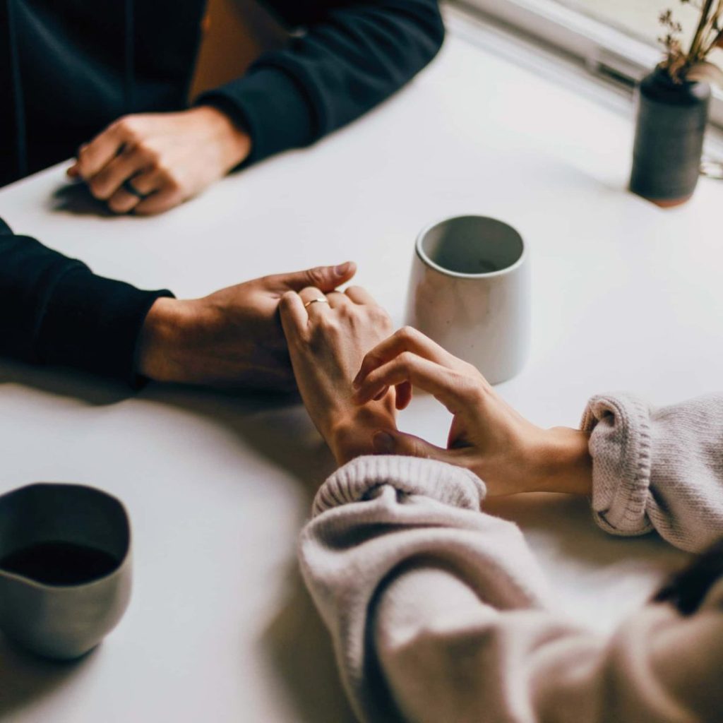 Two people holding hands in support over coffee